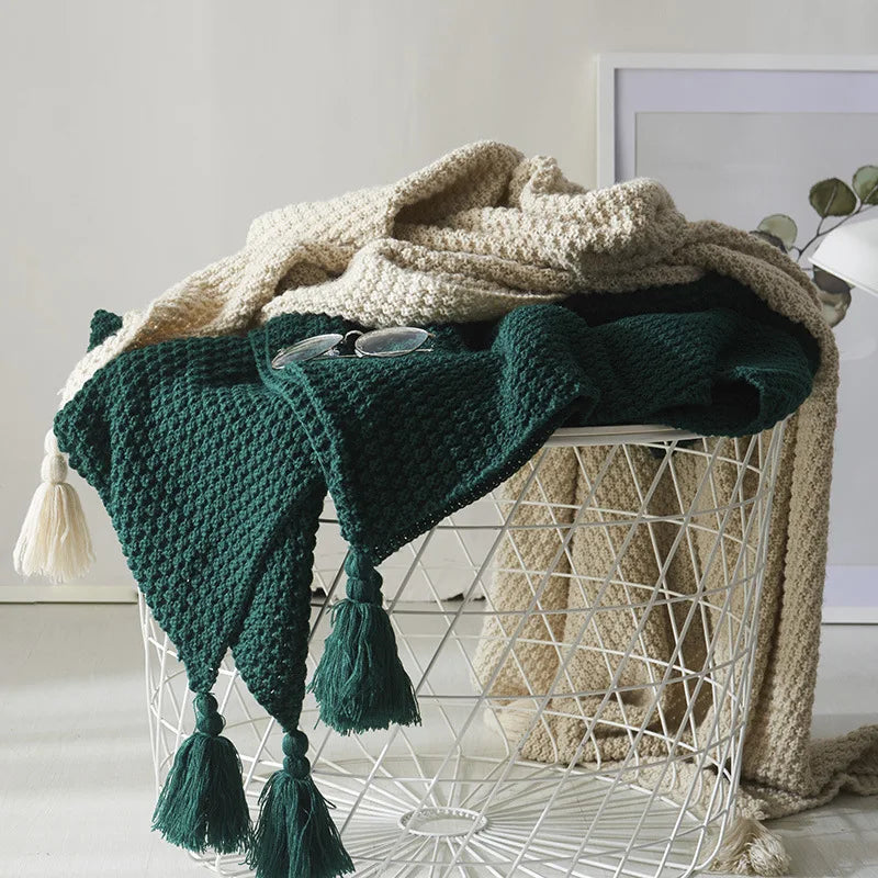 Deep green and beige knitted blankets draped over a white wire basket