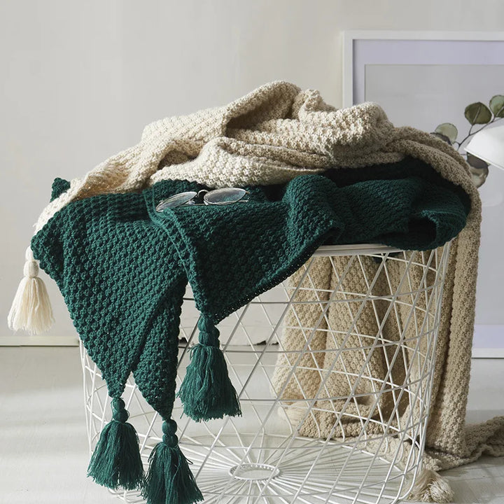 Deep green and beige knitted blankets draped over a white wire basket