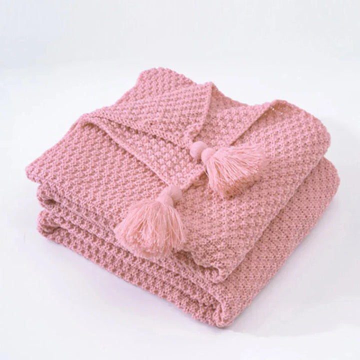 Folded pink knitted blanket with decorative bobbles and tassels