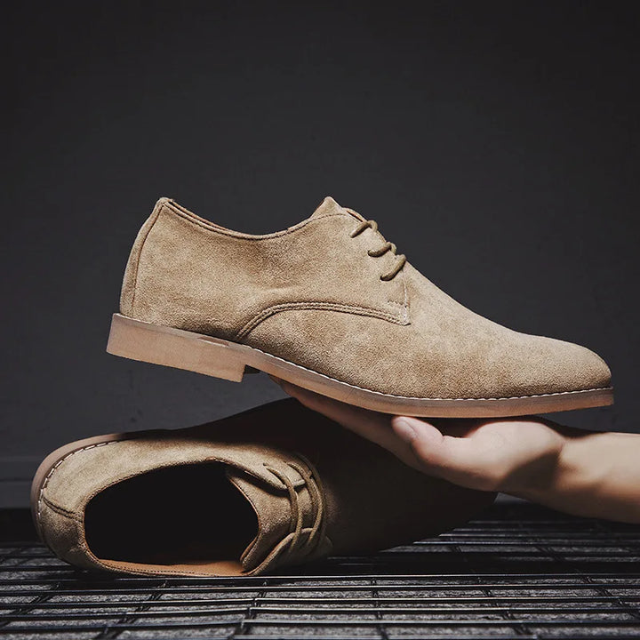 Hand holding a pair of khaki men's dress shoes in studio lighting