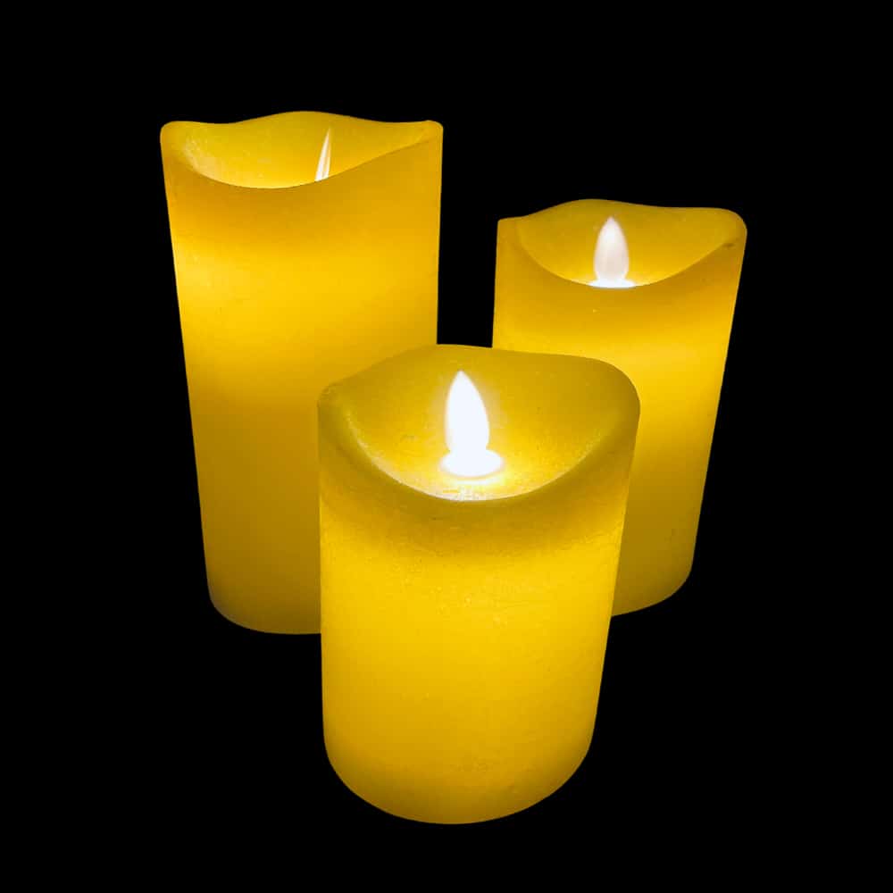 Three yellow LED rustic pillar candles glowing brightly in a dark room
