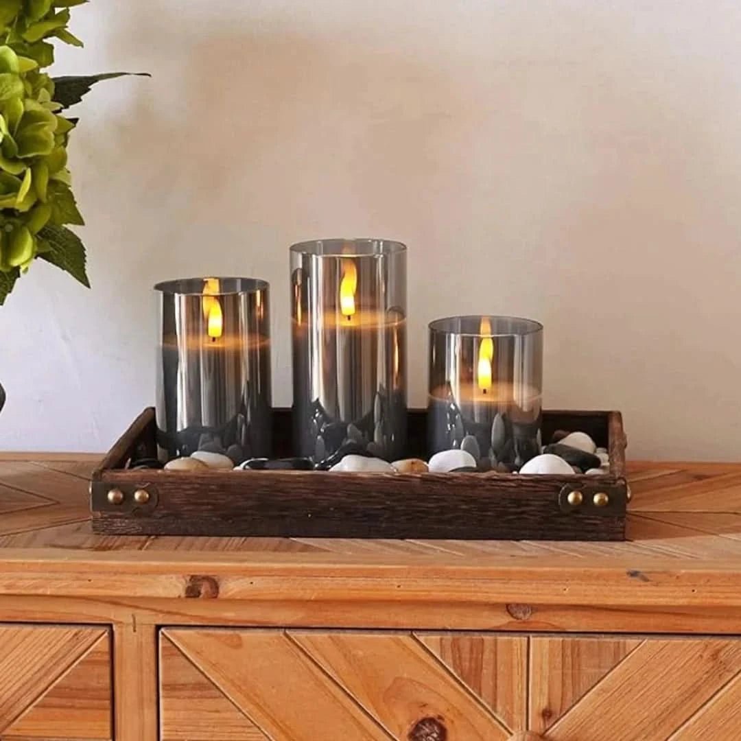 Three gray glass LED flameless candles arranged on a wooden tray with decorative stones.