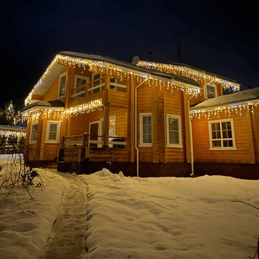 Wooden two-story house illuminated with festive warm LED light curtains in winter snow