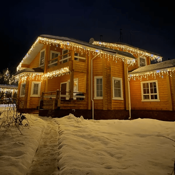 Wooden two-story house illuminated with festive warm LED light curtains in winter snow