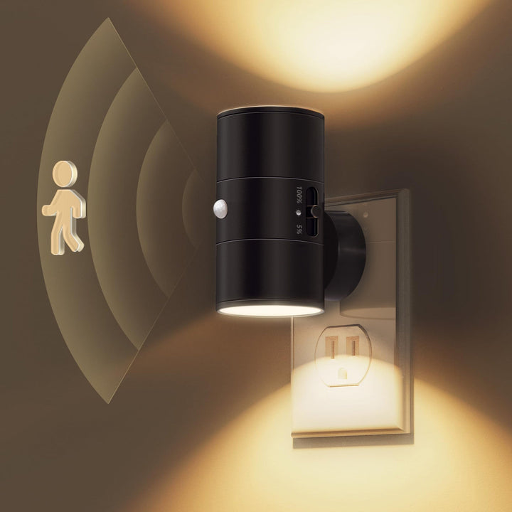 Black plug-in LED motion sensor night light plugged into a wall outlet emitting a warm glow