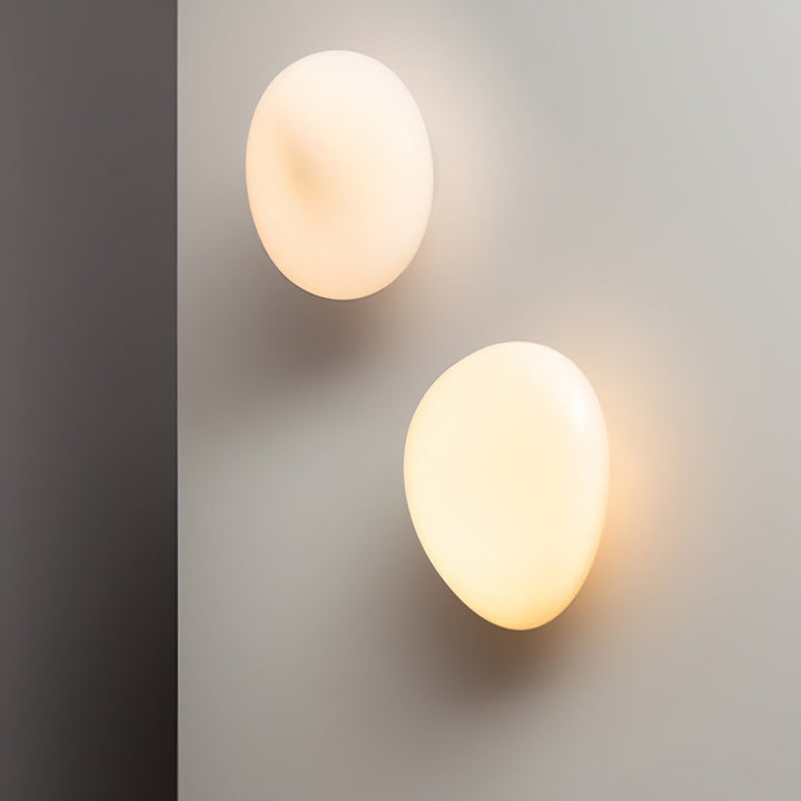 Two white oval glass wall lamps casting a warm illuminating glow in a hallway