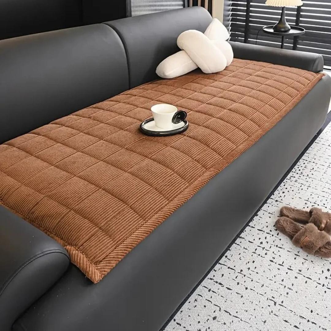 Brown linear quilted couch cover mat displayed on a modern black leather sofa