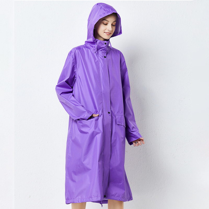 Woman wearing a bright purple long waterproof hooded raincoat standing against a white wall