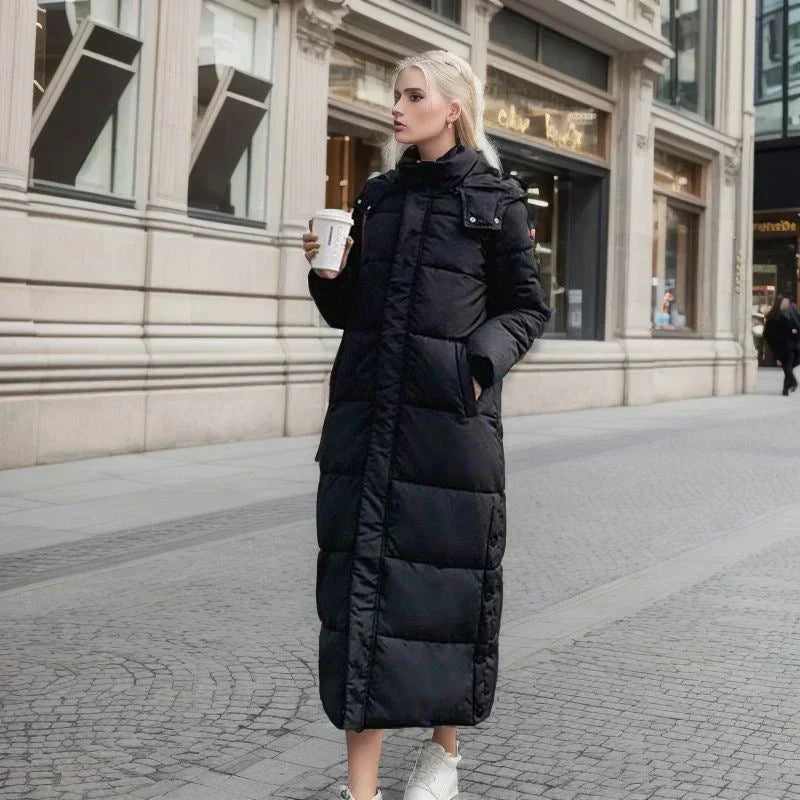 Woman wearing a long black winter coat with a hood walking on a city street.