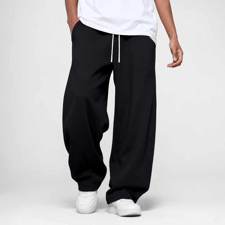 A man wearing black loose and long joggers with white sneakers and a white t-shirt.