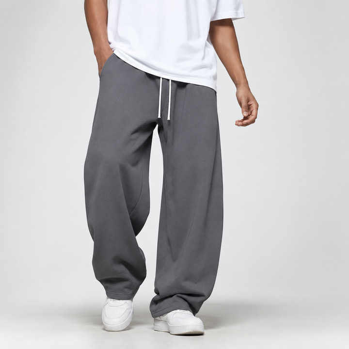 A man wearing dark grey loose and long joggers paired with a white t-shirt.