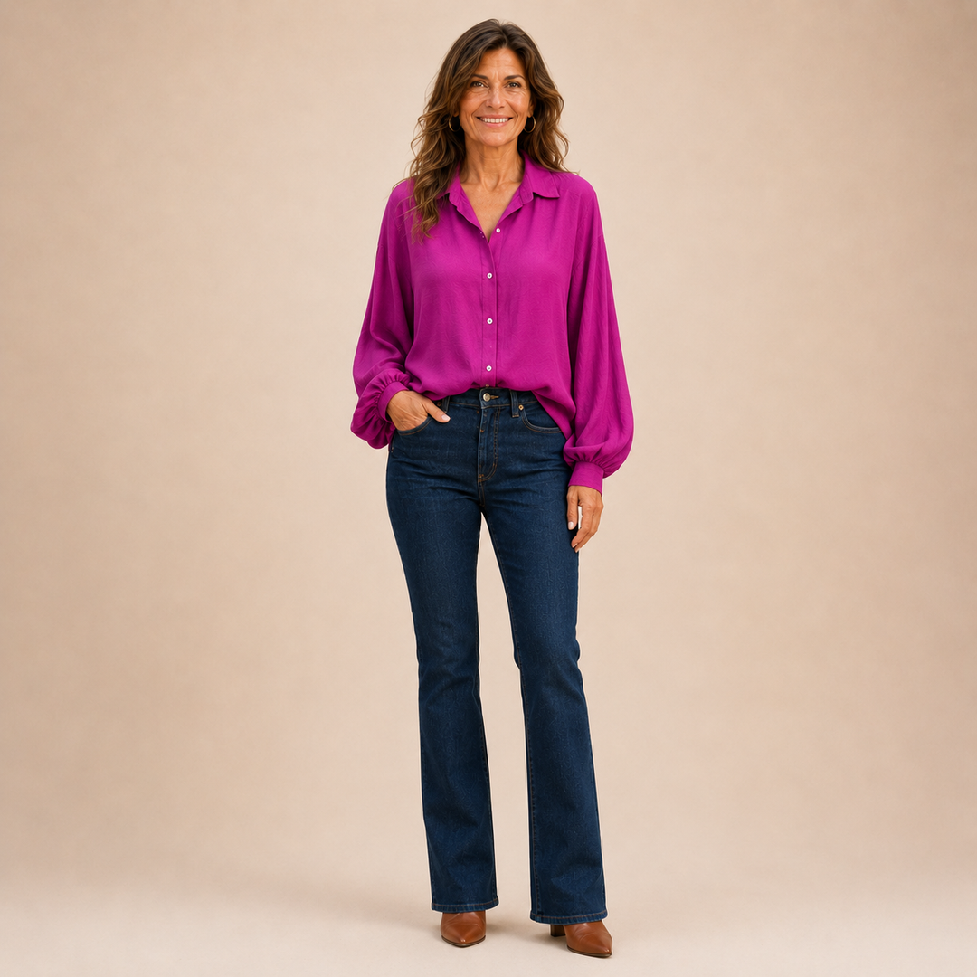 A woman standing confidently in a vibrant purple button down shirt and flared jeans.