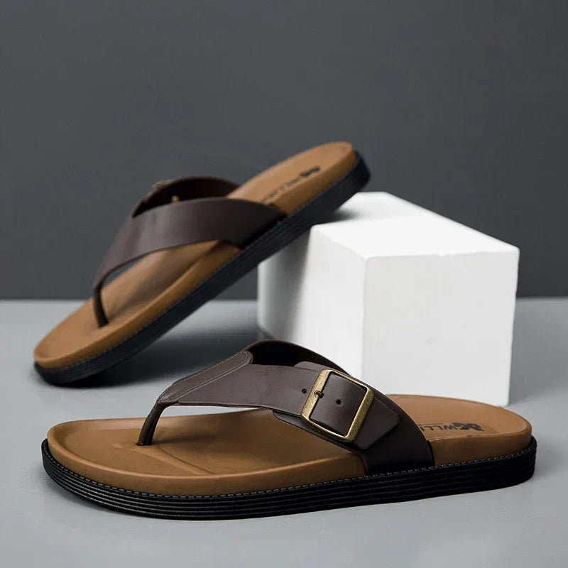 Brown men's thong sandals with buckle detail resting on display block