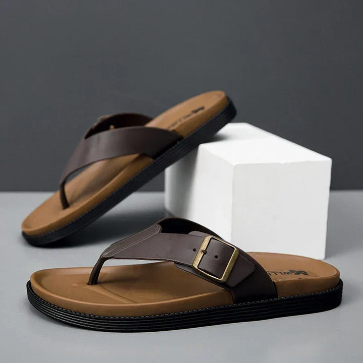 Brown men's thong sandals with buckle detail resting on display block