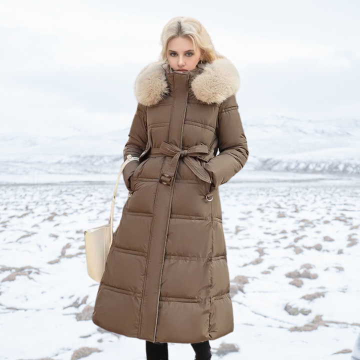Model wearing brown long winter coat with fur hood standing in snow