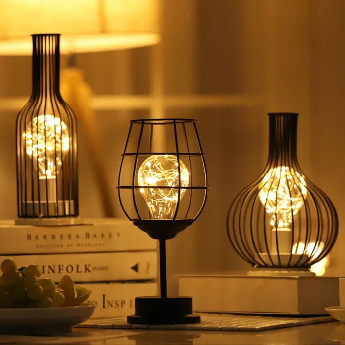 Three black metal wire decorative table lamps lit up on a desk