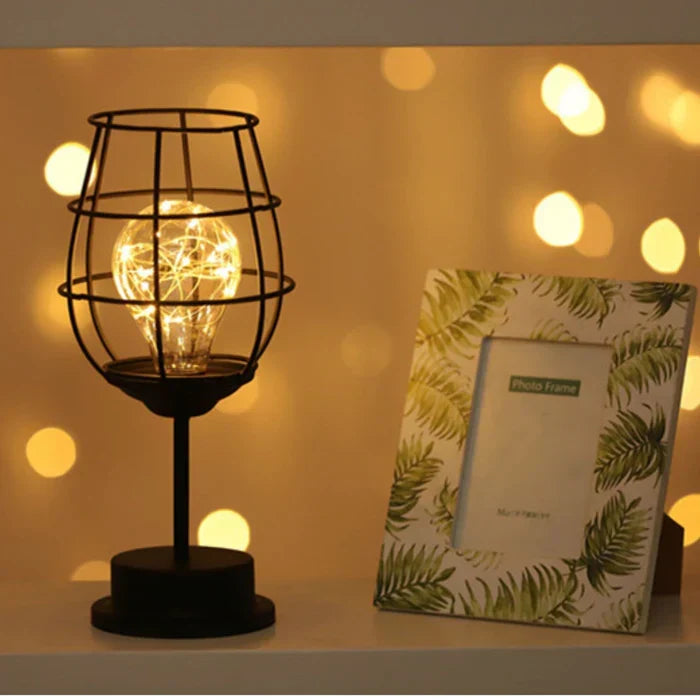 Close up of a wine glass shaped black wire table lamp with warm fairy lights