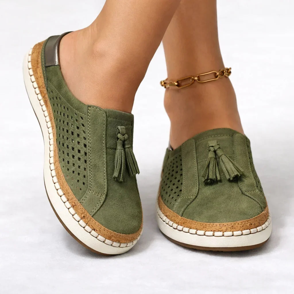 Close-up of green women's slip-on sneaker with tassel and perforated upper worn on foot
