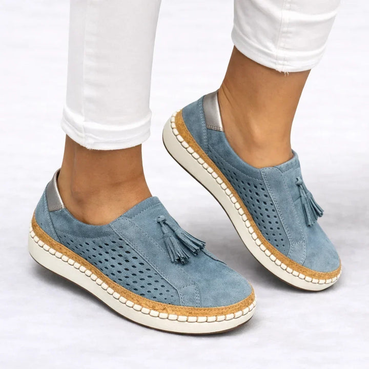 Blue women's slip-on sneaker with tassel and perforated texture styled with white pants