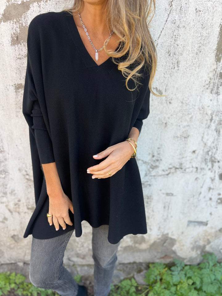 Woman wearing black oversized V-neck long sleeve top with distressed jeans