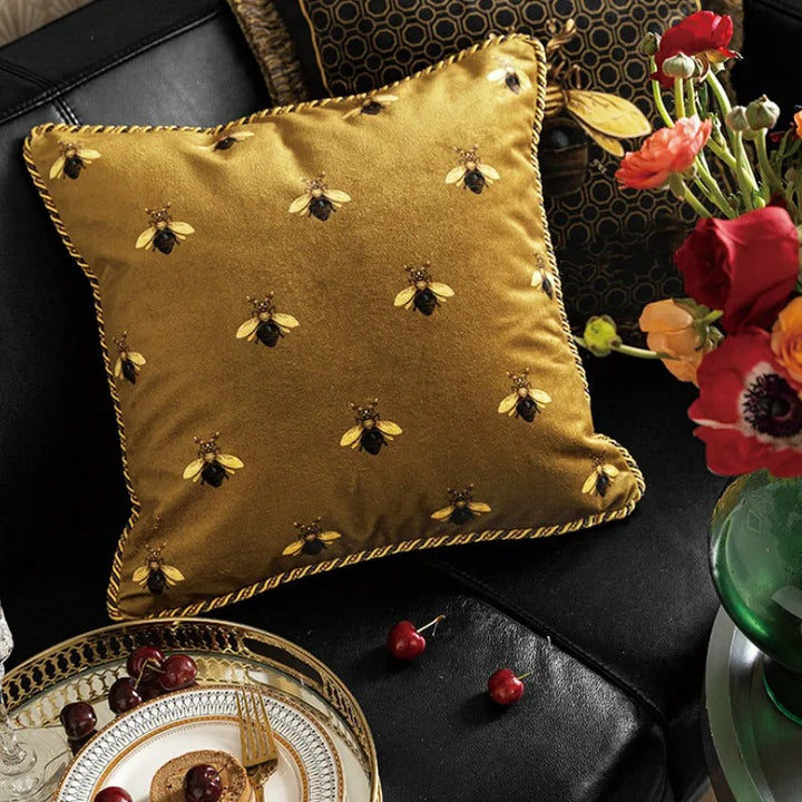 Close-up of a velvet gold bee print cushion cover styled next to fresh flowers