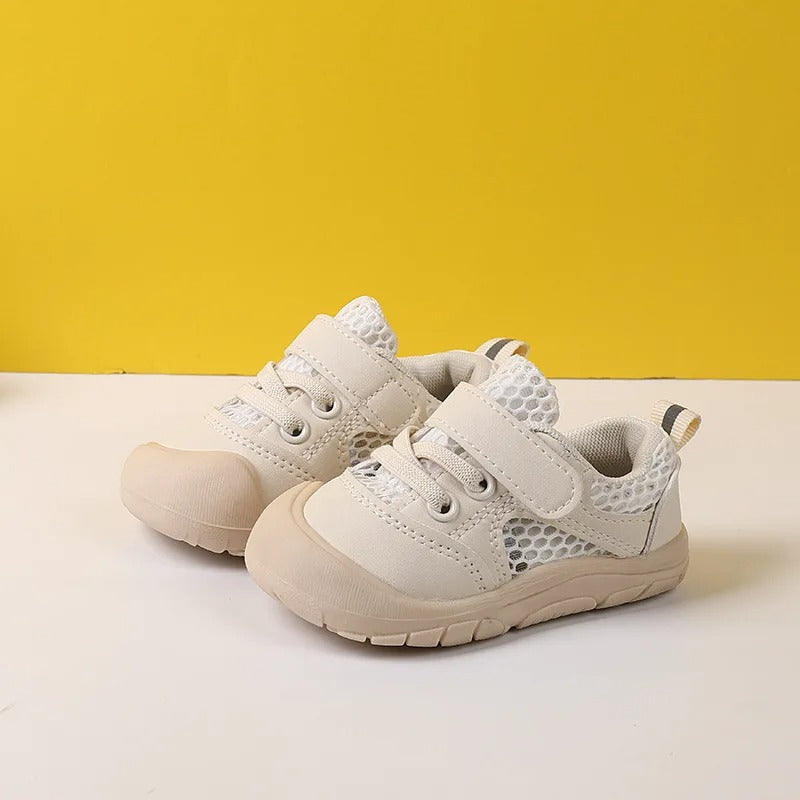 Two beige children's walking shoes showcased side by side on a yellow and white backdrop.