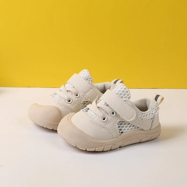 Two beige children's walking shoes showcased side by side on a yellow and white backdrop.