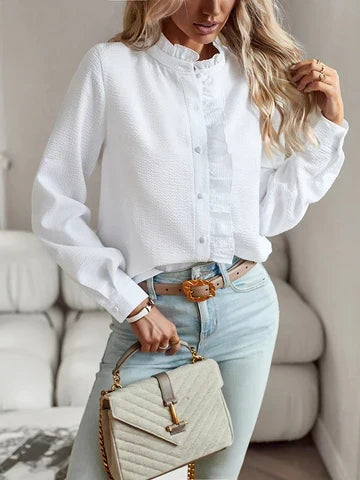 Woman wearing a white long sleeve ruffle blouse paired with jeans and a handbag