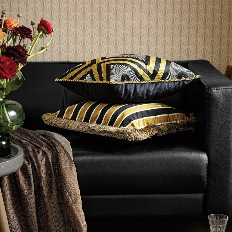 Stacked decorative cushion covers with gold patterns on a dark leather sofa