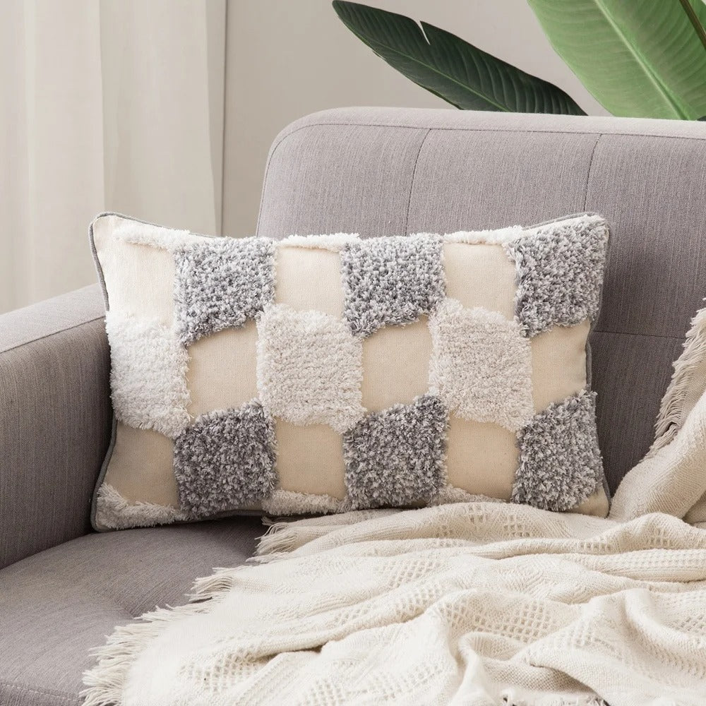 Close-up of a checkered tufted cushion cover resting on a neutral sofa with a textured blanket