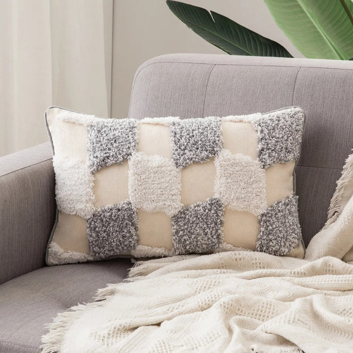 Close-up of a checkered tufted cushion cover resting on a neutral sofa with a textured blanket