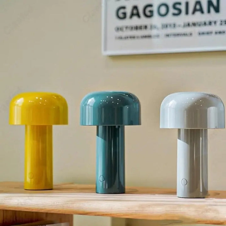 Three wireless retro LED table lamps in yellow, blue, and gray displayed on a wooden shelf.