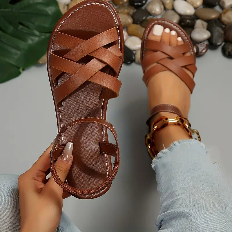 Brown orthopedic strappy summer sandal held in hand against outdoor background