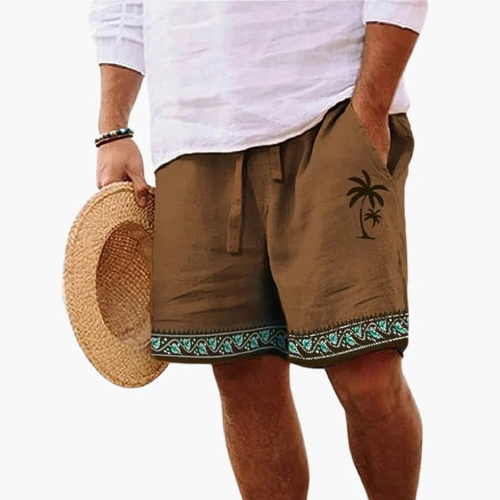 Man wearing brown palm print swimming shorts with white shirt and straw hat