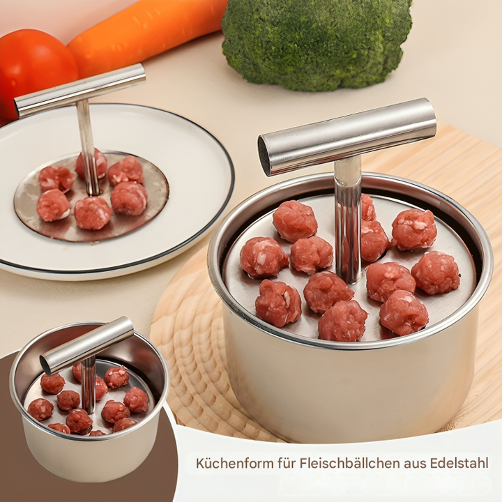Stainless steel meatball maker tool resting next to raw ingredients on a kitchen counter