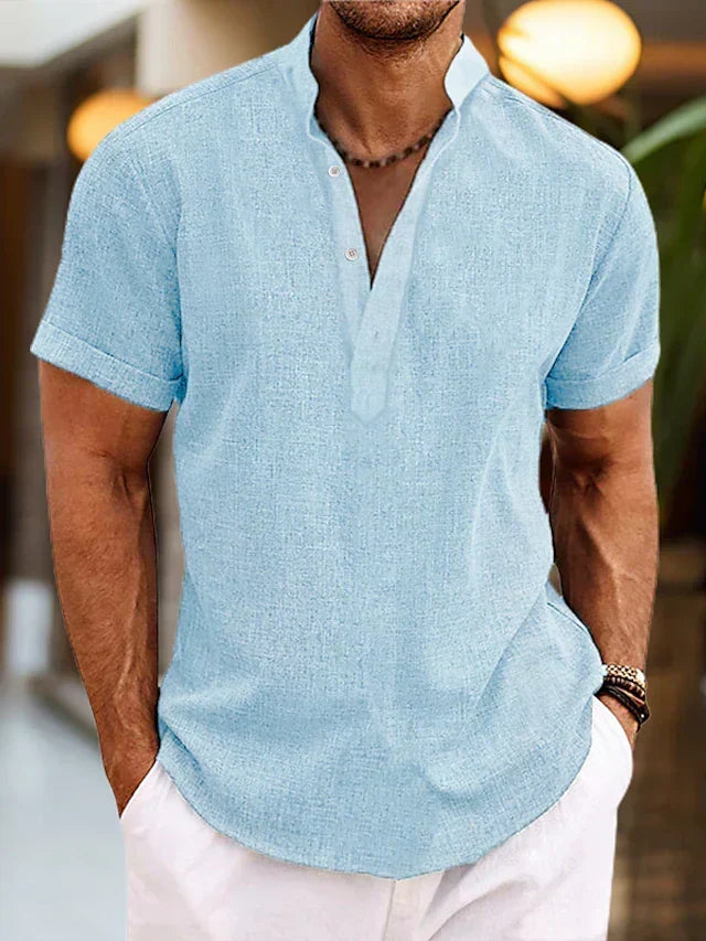 Man wearing a light blue short sleeve Henley shirt with white trousers