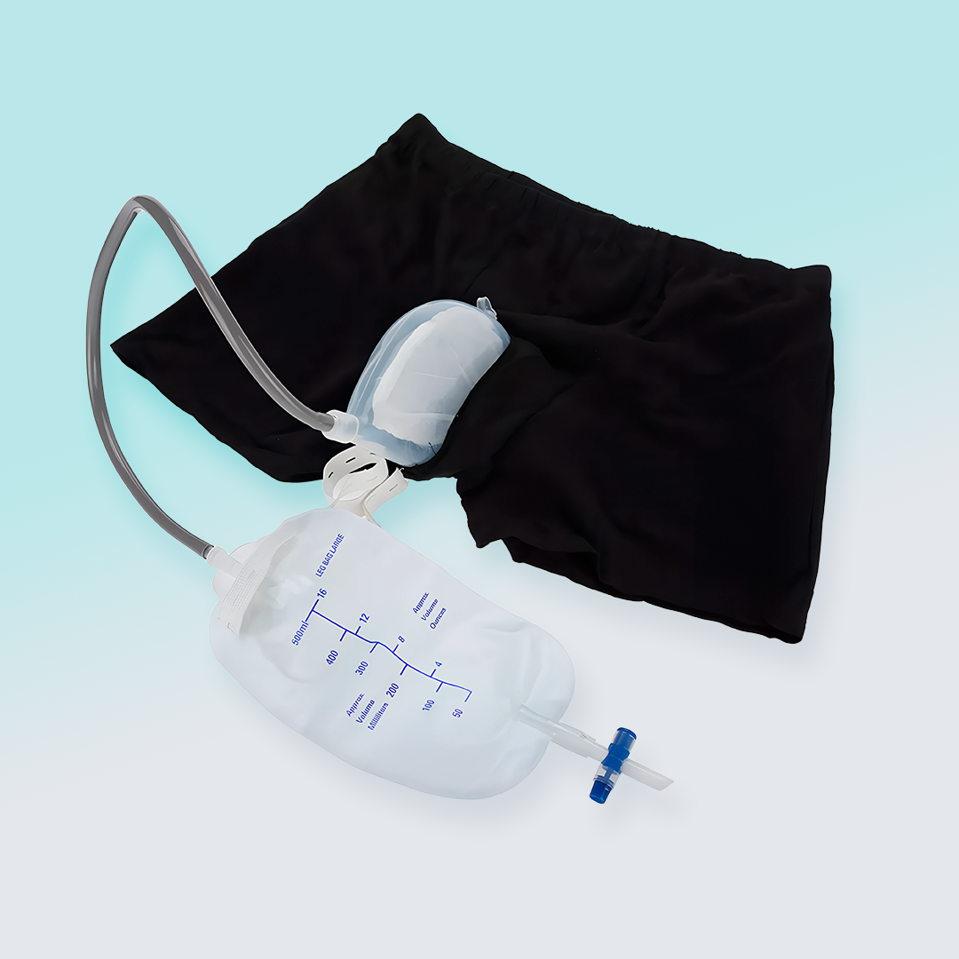 Men's black urinal pants laid out with attached silicone funnel, catheter tubing, and collection bag.