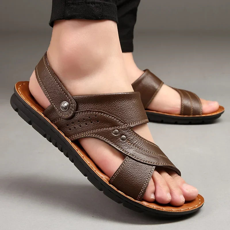 Close-up of a person wearing brown men's sandals with decorative stitching on a grey background.