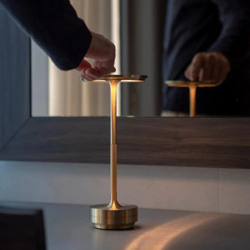 Person adjusting a gold brass touch-control rechargeable table lamp indoors