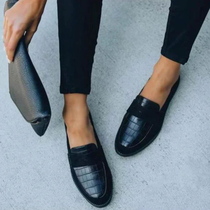 Women wearing black Mila loafers with a matching clutch bag