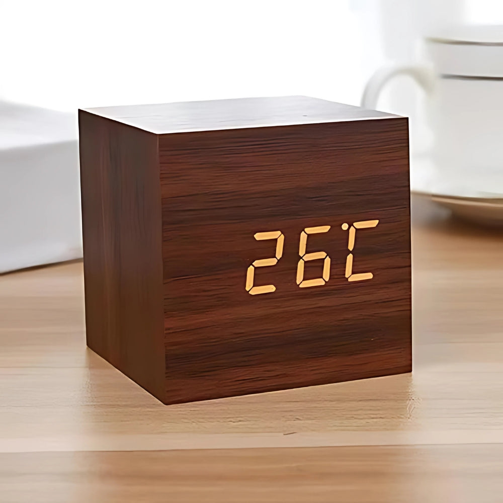 Modern cube LED alarm clock in dark wood finish displaying temperature on a wooden desk