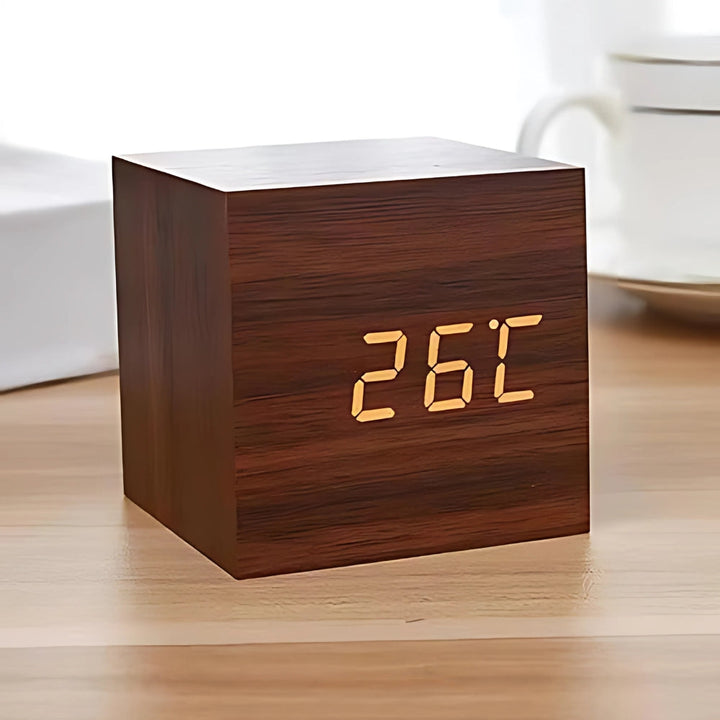 Modern cube LED alarm clock in dark wood finish displaying temperature on a wooden desk