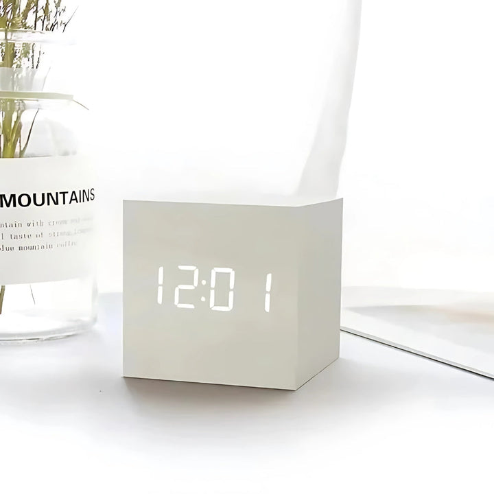 Modern cube LED alarm clock in ivory white finish placed next to a vase with dried flowers