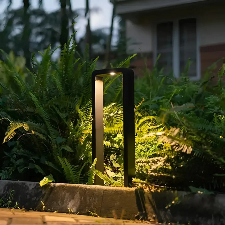 Modern LED garden light column glowing softly amidst lush green ferns along a walkway