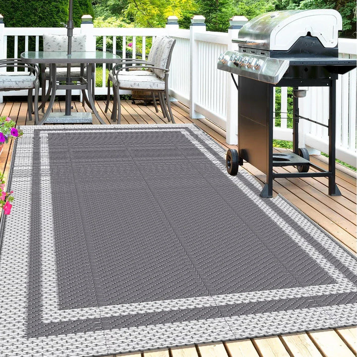 Modern rectangular outdoor mat laid out on a wooden deck next to a patio table and grill