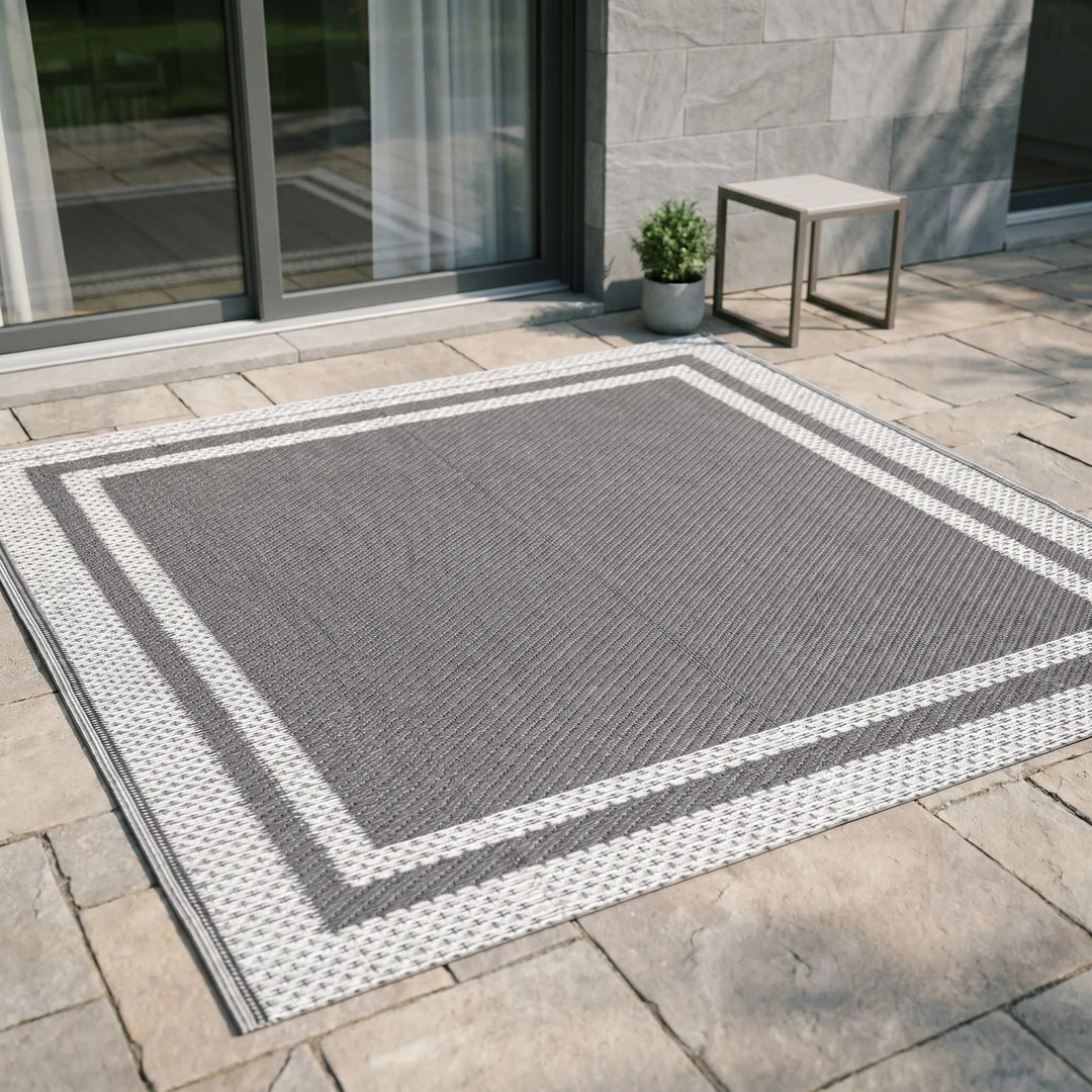 Gray and white geometric outdoor rug placed on stone patio tiles near a sliding glass door