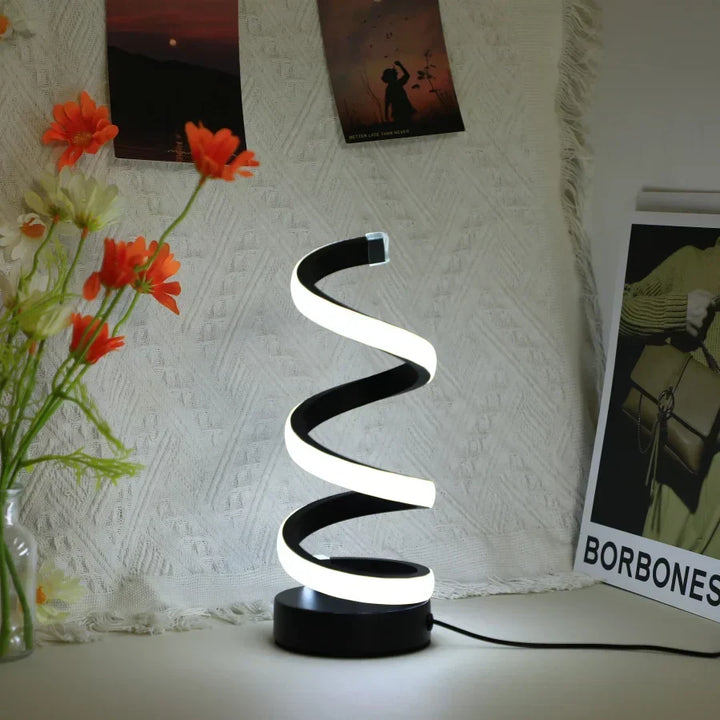Modern S-shaped black desk lamp illuminated brightly against a textured fabric background