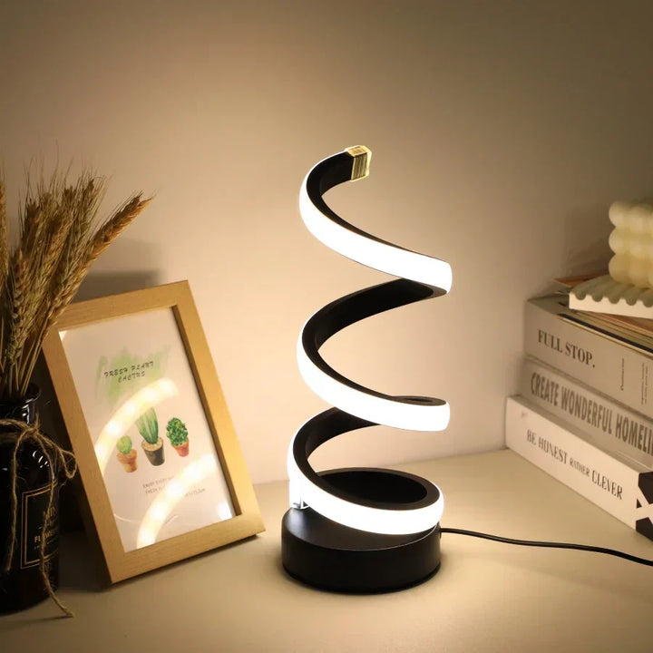 Modern S-shaped black desk lamp emitting a warm cozy glow on a desk setup