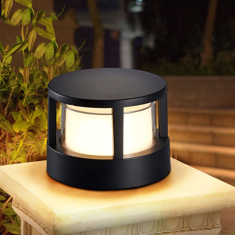 Round black aluminium LED outdoor pillar light emitting warm glow on stone pedestal