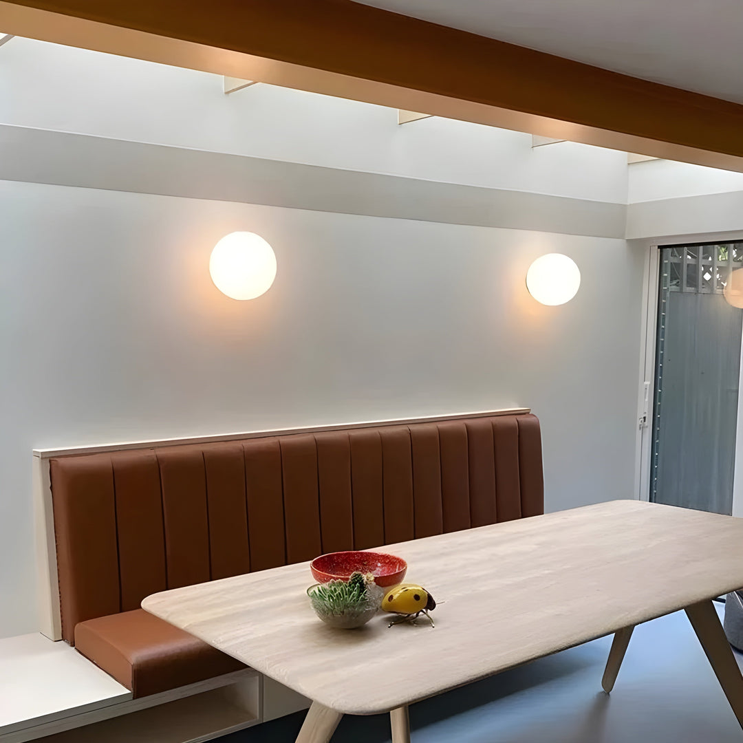 Elegant spherical wall lamps mounted on a white wall above a dining table in a bright modern home